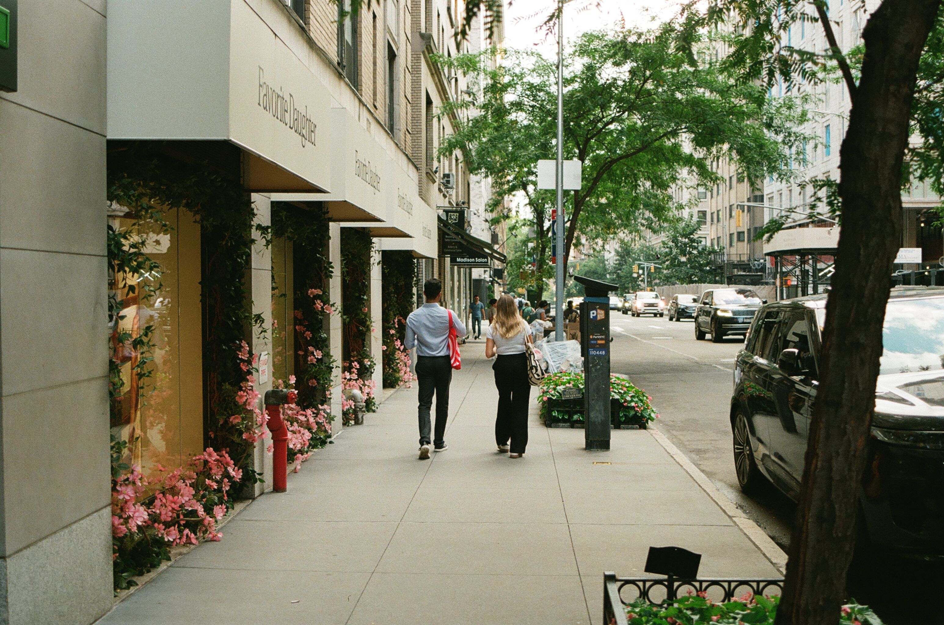 Two people walking along a flower-lined sidewalk