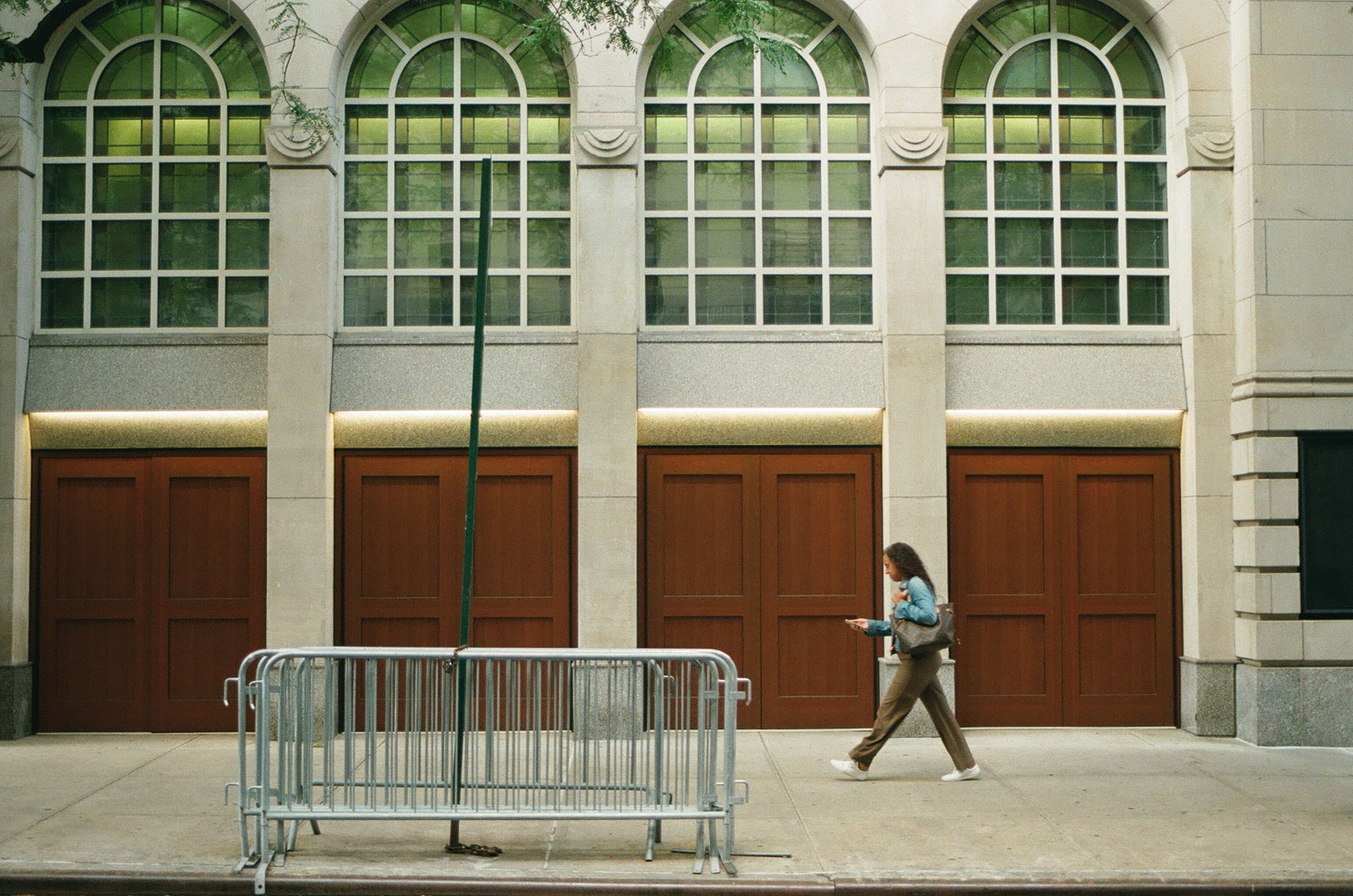 Pedestrian passing a facade of repeating arched windows and doors