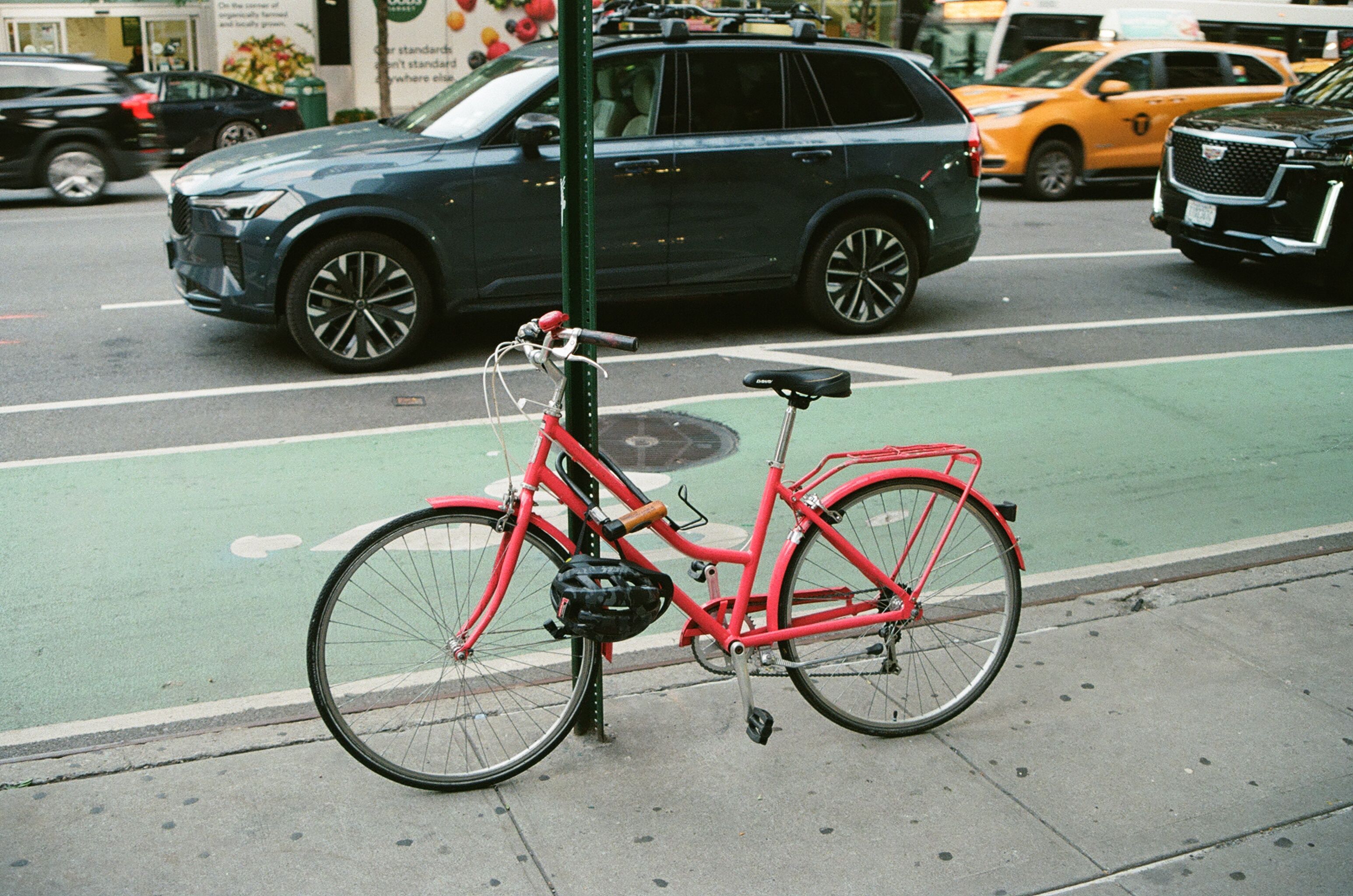 Red bicycle parked beside a busy avenue