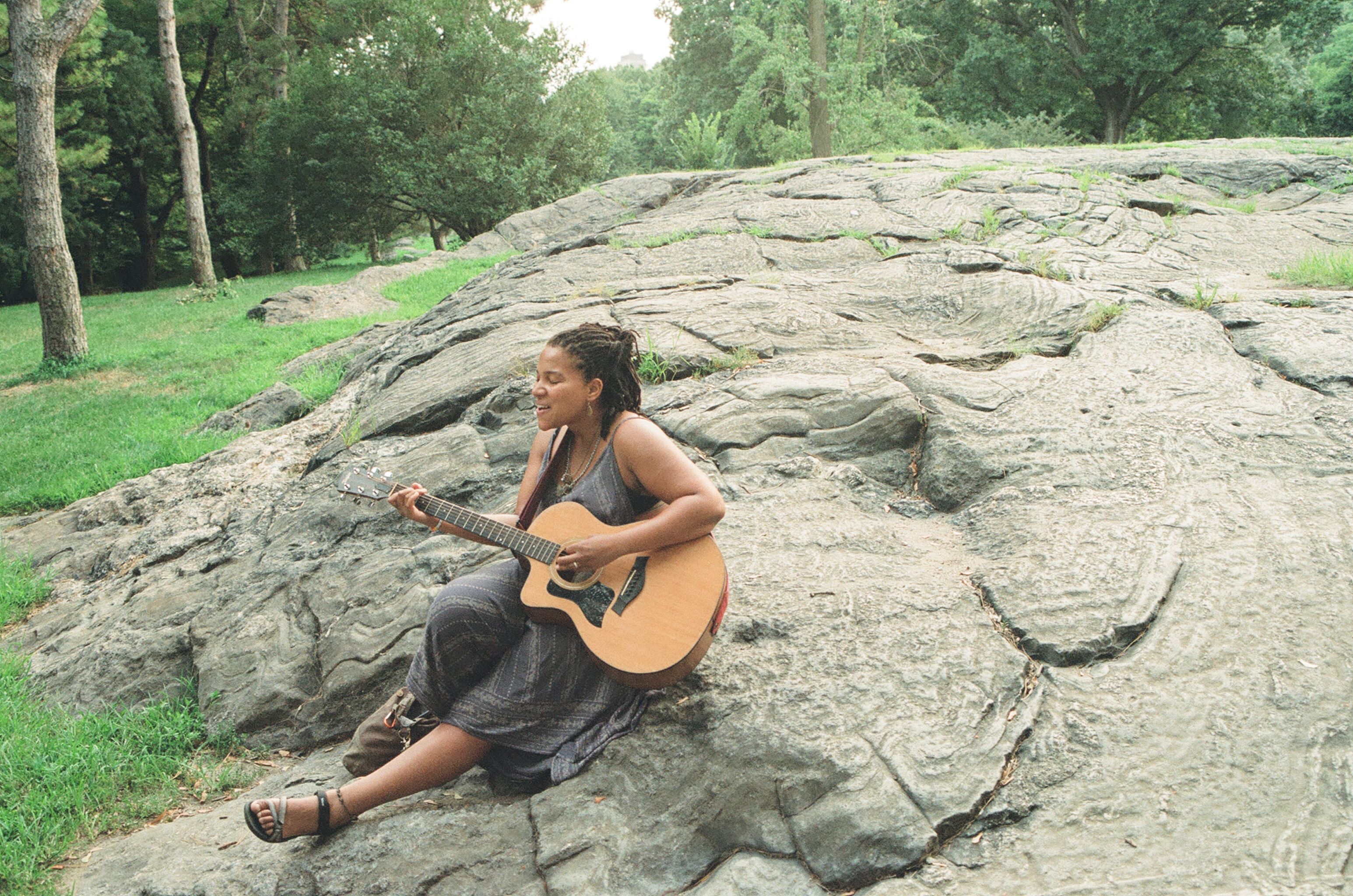 A guitarist seated on a rock in Central Park