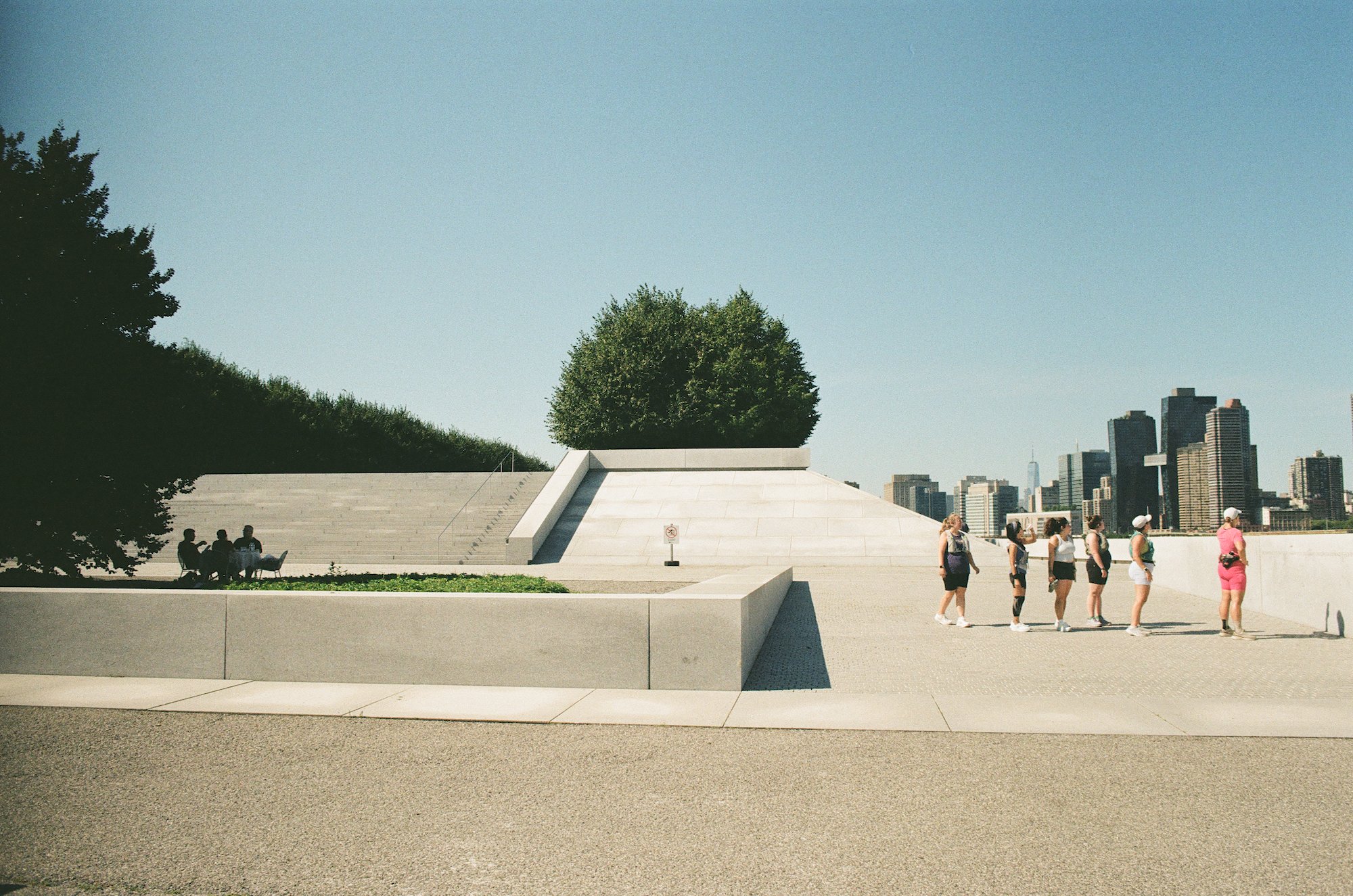 Visitors crossing the white memorial plaza with the Manhattan skyline beyond