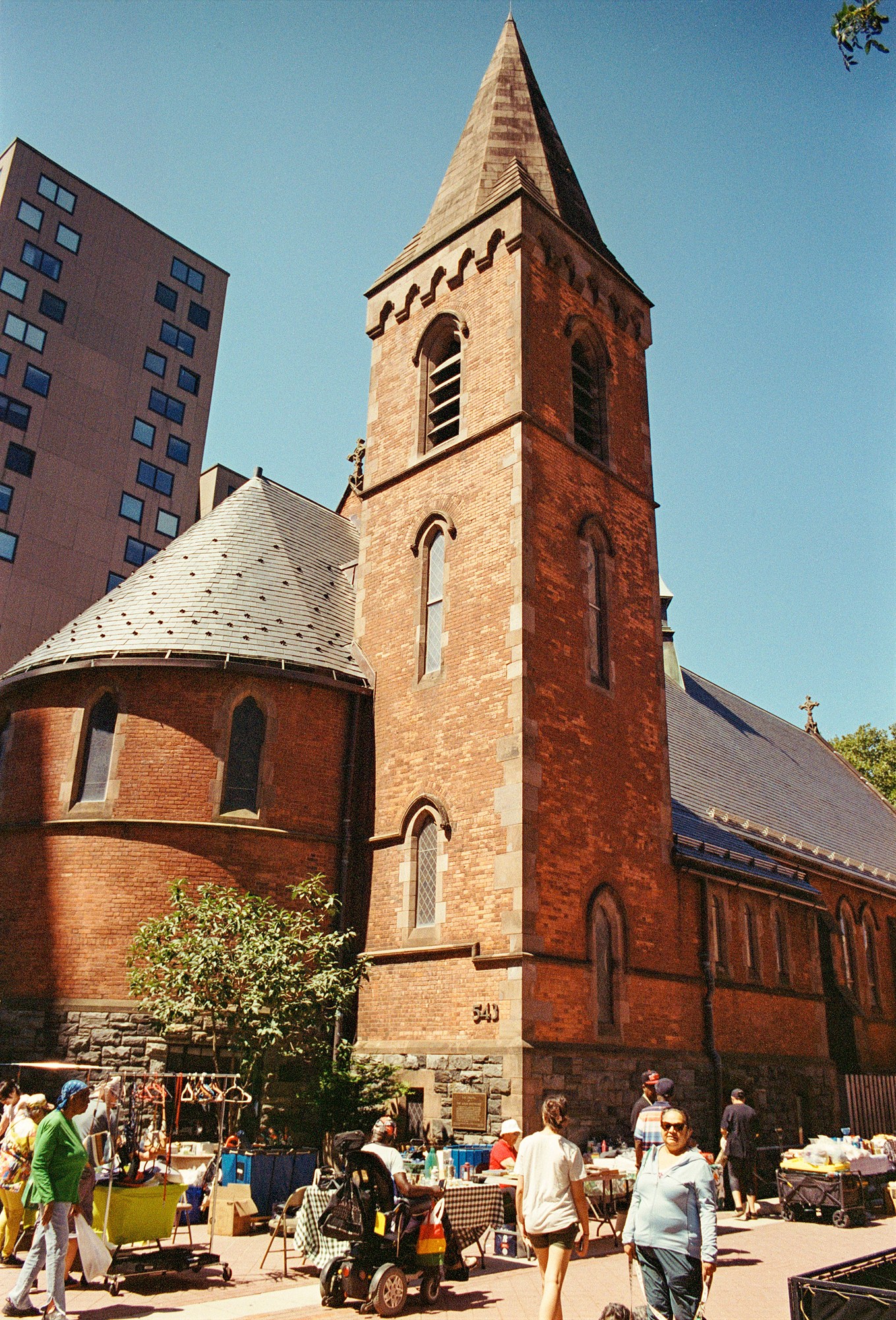 Brick church tower rising above a neighborhood market and its visitors