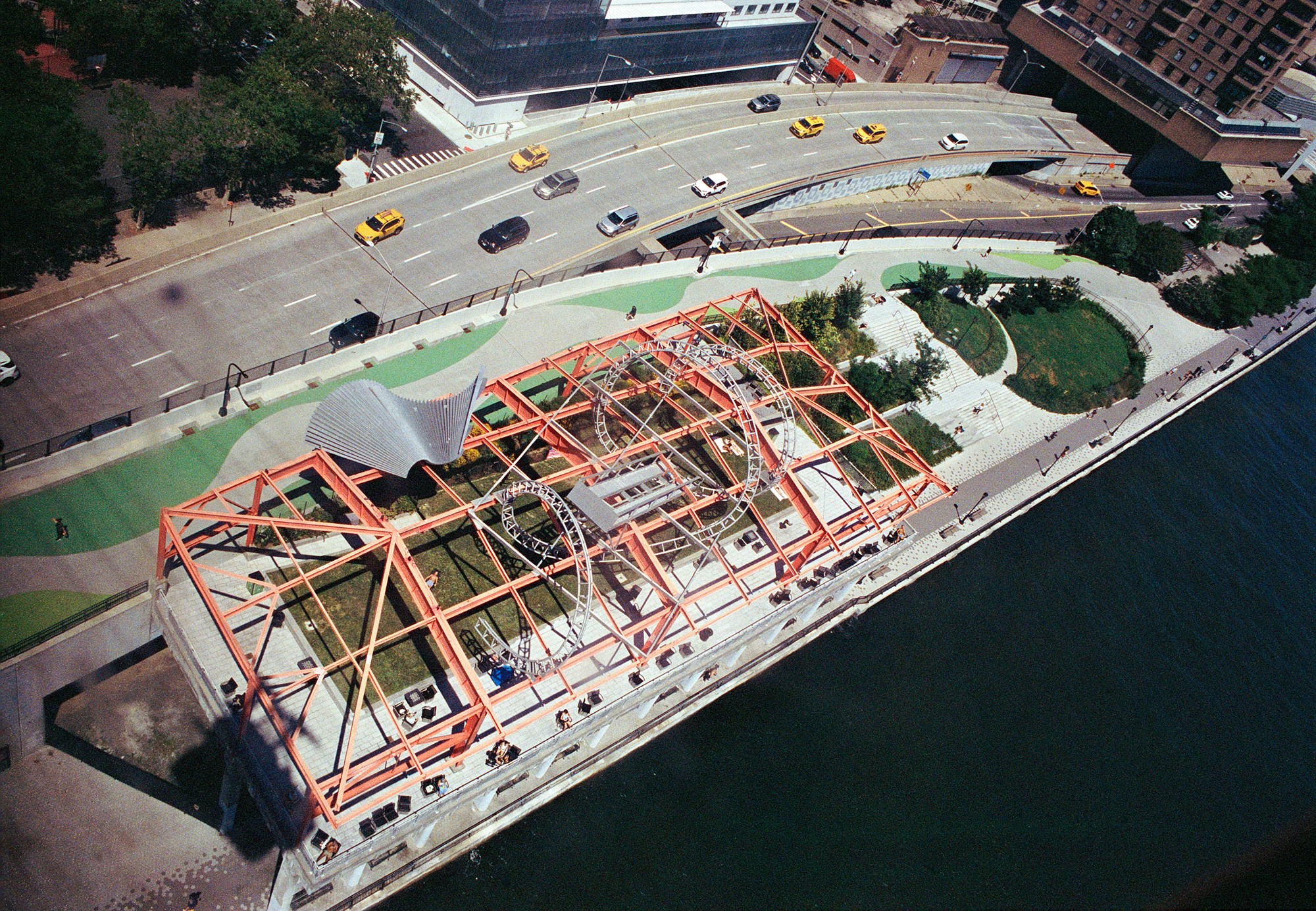 Aerial view of a red steel art installation, waterfront park, and passing traffic