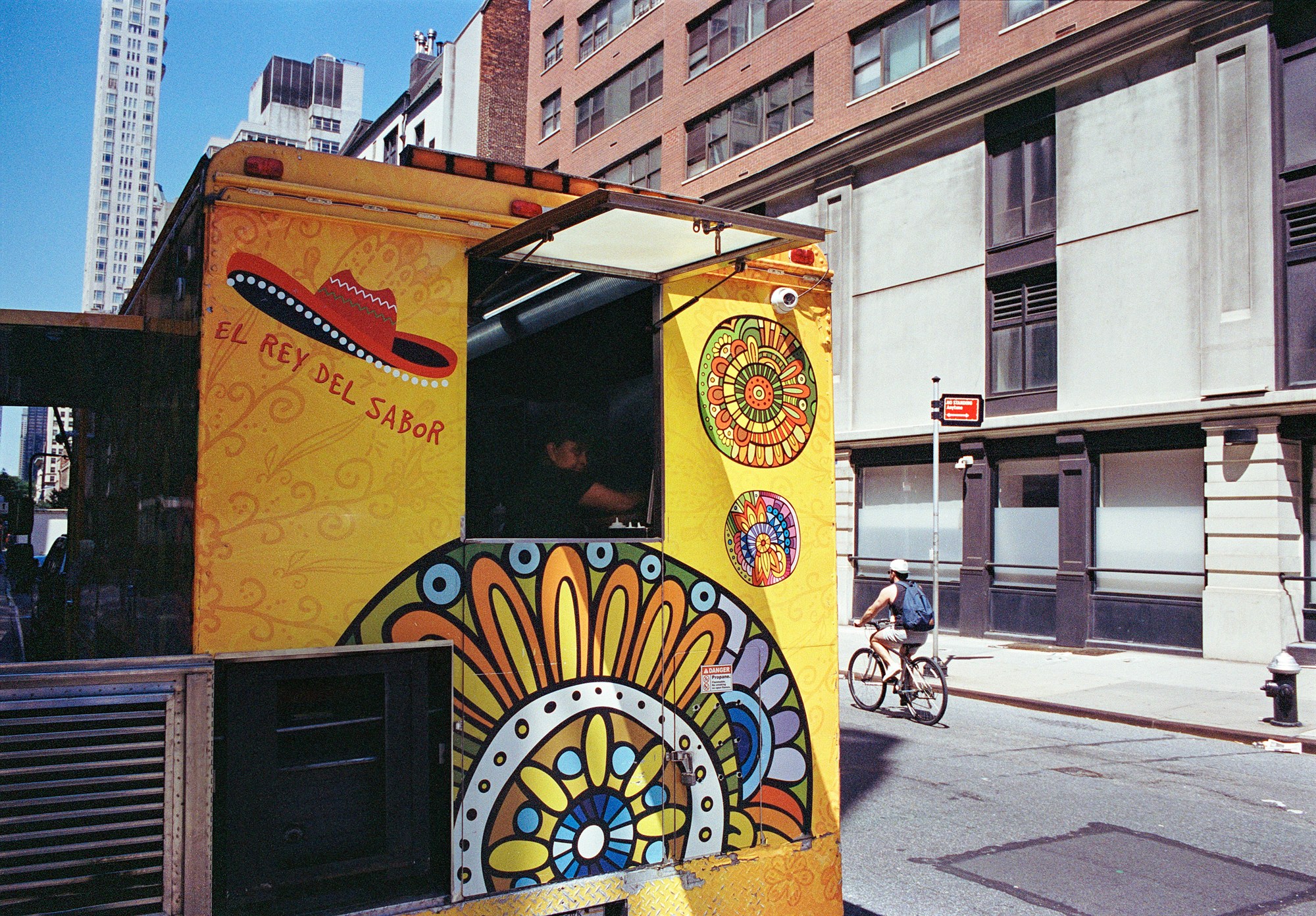 Brightly painted food cart with its vendor and a cyclist passing behind it
