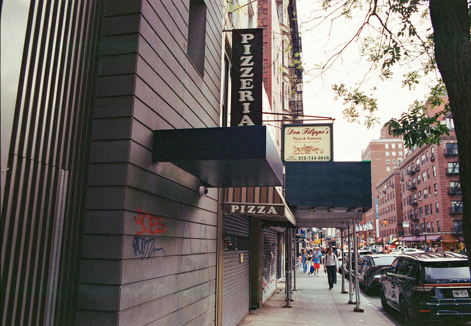 Pizzeria signs and pedestrians beneath sidewalk scaffolding