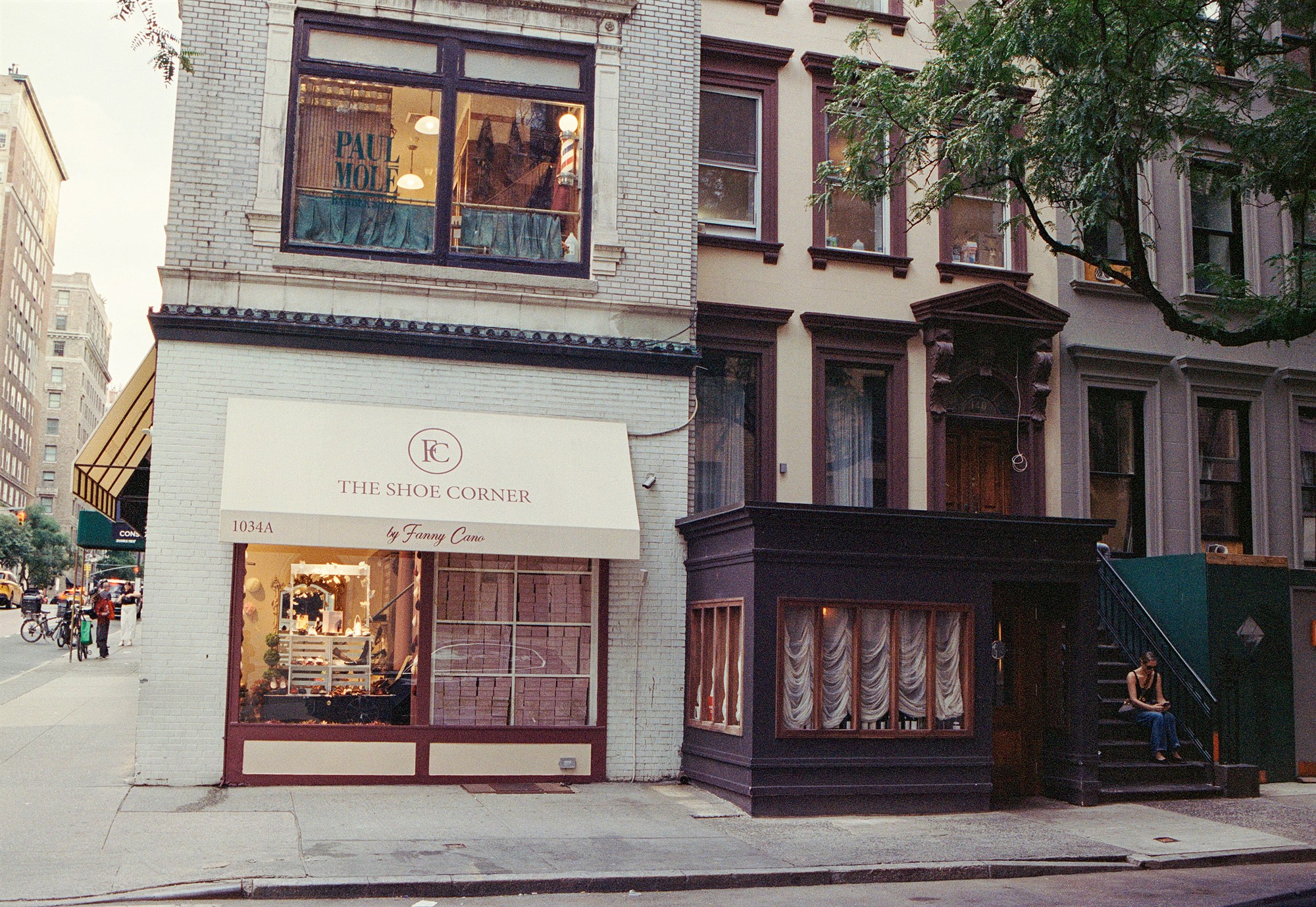 Woman seated on brownstone steps beside a corner shoe shop